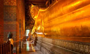 Stor gyllene liggande Buddha i ett tempel i Bangkok. En mindre Buddha-staty står till vänster.