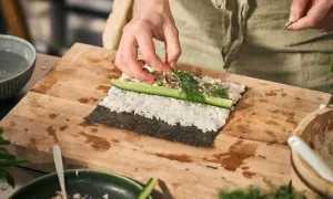 Händer lägger dill på ris och gurka för ett sushi recept.