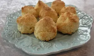 Små, gyllene kokostoppar ligger uppradade på en vacker ljusblå tallrik. Perfekta att baka med detta kokostoppar recept!