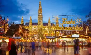 En livlig julmarknad i Europa med folk som strosar bland ljus och stånd framför en vackert upplyst byggnad.