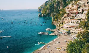 Färgstark by klättrar uppför klipporna vid sorrentohalvön, med båtar på det turkosa havet och en strand full av folk.