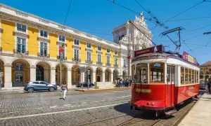 Röd spårvagn i Lissabon, perfekt för en interrail eu-resa. Gula byggnader och en triumfbåge i bakgrunden.