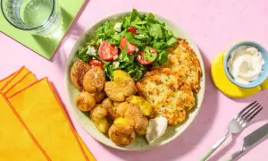 En tallrik med krispiga potatisar, en fräsch sallad med tomat och fetaost, och gyllene fiskkakor. Ett perfekt sallad recept för en lätt lunch.