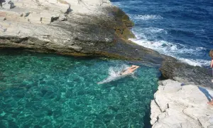 En person simmar i turkost vatten vid en klippig kust på Thassos, Grekland.