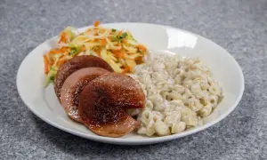 En tallrik med stuvade makaroner, stekt falukorv och en fräsch sallad. En klassisk svensk måltid.
