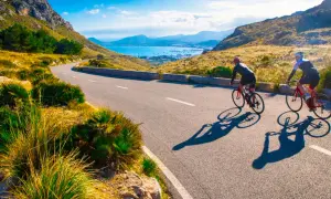 Två cyklister njuter av en solig dag med att cykla på Mallorca, med en vacker vy över havet och bergen.