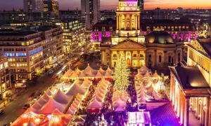 En livlig julmarknad i Berlin med tält, en stor julgran och upplysta byggnader i skymningen.