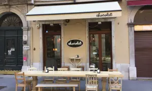Uteservering vid ett chokladcafé i Trieste, Italien. Långt bord med stolar och bänkar framför butiken.