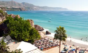 En solig strand med parasoller och badande människor. Vackert turkost hav och berg i bakgrunden. Spanien temperatur året runt är perfekt för detta.
