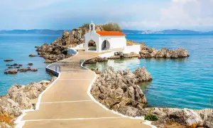 En vit kyrka med orange tak på en klippig ö, nås via en gångväg. Vackert vid Skiathos, Grekland.