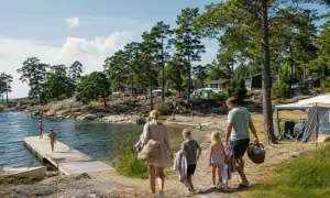 Familj på väg mot vattnet för en härlig sommarsemester med barn. Sol, bad och campingliv vid en svensk sjö.