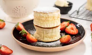 Två fluffiga japanska pannkakor staplade på en tallrik med färska jordgubbar och pudersocker.