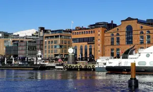En del av Oslo med moderna byggnader, en gammal tegelbyggnad med ett stort klocktorn vid vattnet och båtar.