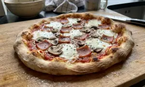 En hemgjord pizza med skinka och champinjoner, perfekt för ett mysigt hemmakväll. Ett enkelt hemgjord pizza recept att prova!