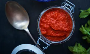En burk med kryddig mojo rojo bredvid en sked och färska örter.