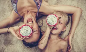 Glad mamma och barn på stranden i Thailand med drakfrukt.