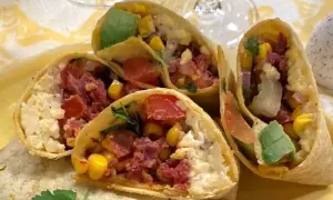 En närbild på en frukost burrito fylld med majs, tomat, avokado och kött.