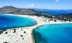 En vit sandstrand med turkost vatten och en segelbåt vid **Platanias, Kreta**. Berg i bakgrunden.