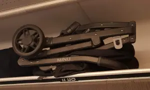 En hopfälld barnvagn, märkt "MINU", ligger som handbagage på en hylla.