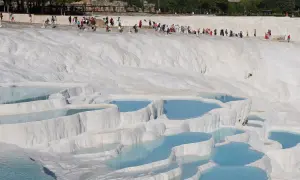 Turister njuter av de turkosa bassängerna vid Pamukkale i Turkiet, ett naturligt underverk av vita kalkstensterrasser.