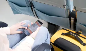 Person visar boardingkort på mobilen i ett flygplanssäte. Gul Samsonite-väska bredvid. Smidigt med digitala biljetter för ditt ving flygbolag.