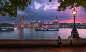 En kvinna ser på Houses of Parliament vid solnedgången. En båt glider förbi på Themsen, en ikonisk vy över London stadsdelar.