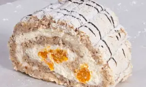 En bit av en Budapest bakelse med vispgrädde och kanderad frukt, pudrad med florsocker och dekorerad med choklad.
