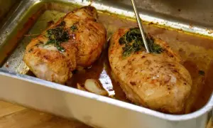 Två saftiga kycklingfiléer i en ugnsform, redo att dras isär till pulled chicken. En termometer mäter temperaturen.