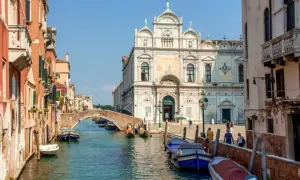En vacker vy av en del av Venedig med kanaler, broar och historiska byggnader. Båtar ligger förtöjda längs kanalen.