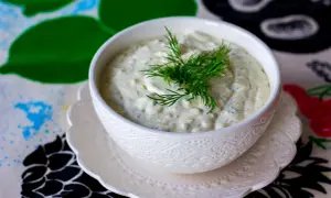 Krämig skolans fisksås med dill, serverad i en vit skål på ett mönstrat underlägg.