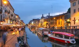 Kvällsliv vid Navigli i Milano. Folk promenerar längs kanalen, båtar ligger vid kaj och restauranger lyser upp.