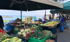 Frukt- och grönsaksstånd vid marknad i Chania. Färska varor som majs, broccoli och tomater säljs med havet i bakgrunden.