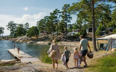 Familj på väg mot vattnet för en härlig sommarsemester med barn. Sol, bad och campingliv vid en svensk sjö.