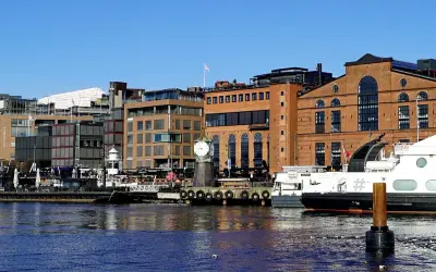 En del av Oslo med moderna byggnader, en gammal tegelbyggnad med ett stort klocktorn vid vattnet och båtar.