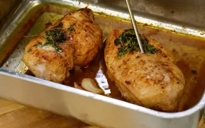 Två saftiga kycklingfiléer i en ugnsform, redo att dras isär till pulled chicken. En termometer mäter temperaturen.