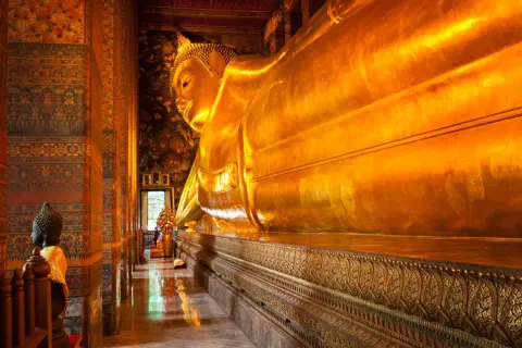 Stor gyllene liggande Buddha i ett tempel i Bangkok. En mindre Buddha-staty står till vänster.