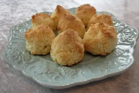 Små, gyllene kokostoppar ligger uppradade på en vacker ljusblå tallrik. Perfekta att baka med detta kokostoppar recept!