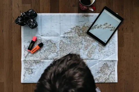 Planerar en resa ensam. Karta, kamera, surfplatta och överstrykningspennor ligger redo.