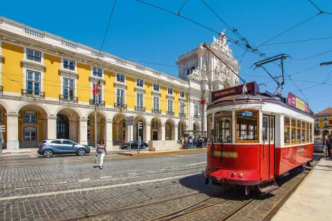 Röd spårvagn i Lissabon, perfekt för en interrail eu-resa. Gula byggnader och en triumfbåge i bakgrunden.