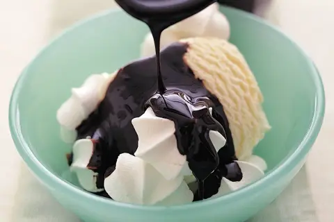 En skål med vaniljglass och visp täcks av glansig chokladsås. Ett perfekt chokladsås recept för en lyxig dessert.