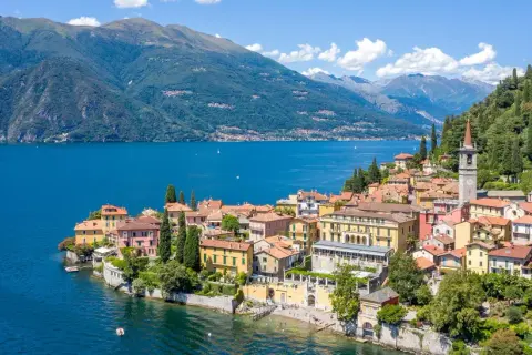 Färgstark by vid en blå sjö i norra Italien, med gröna berg i bakgrunden.