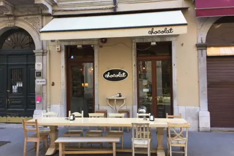 Uteservering vid ett chokladcafé i Trieste, Italien. Långt bord med stolar och bänkar framför butiken.