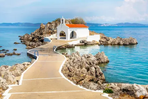 En vit kyrka med orange tak på en klippig ö, nås via en gångväg. Vackert vid Skiathos, Grekland.