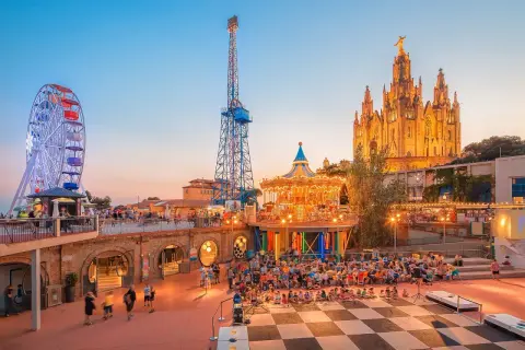 Tivoli i solnedgången med pariserhjul, karusell och en imponerande kyrka. Perfekt för Barcelona aktiviteter med familjen.