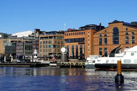 En del av Oslo med moderna byggnader, en gammal tegelbyggnad med ett stort klocktorn vid vattnet och båtar.