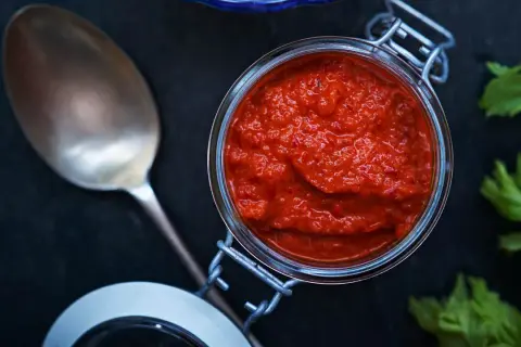 En burk med kryddig mojo rojo bredvid en sked och färska örter.