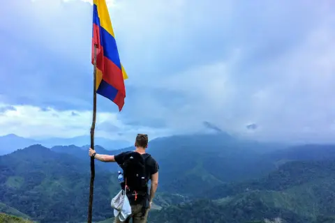 Vandrare med Colombias flagga på en bergstopp. Trots att en resa till Colombia kan verka farligt, bjuder landet på otroliga vyer.