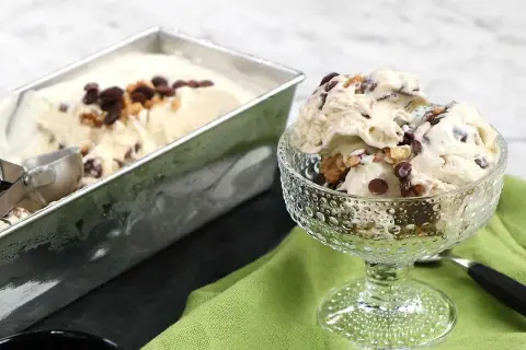 En skål med krämig nicecream banan, toppad med chokladbitar och nötter. Bredvid står en form med mer glass.