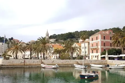 Hamnen i Hvar, Kroatien, med palmer, färgglada hus och små båtar i det turkosa vattnet.
