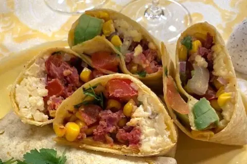 En närbild på en frukost burrito fylld med majs, tomat, avokado och kött.